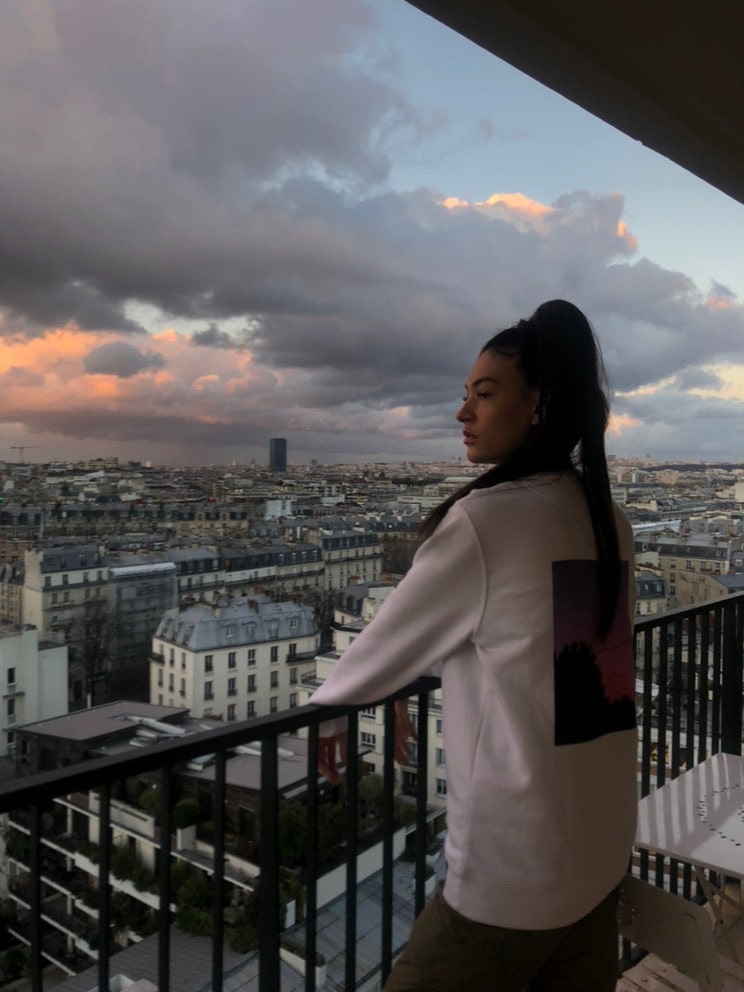A woman standing on a balcony in Paris wearing a Huntt sweatshirt