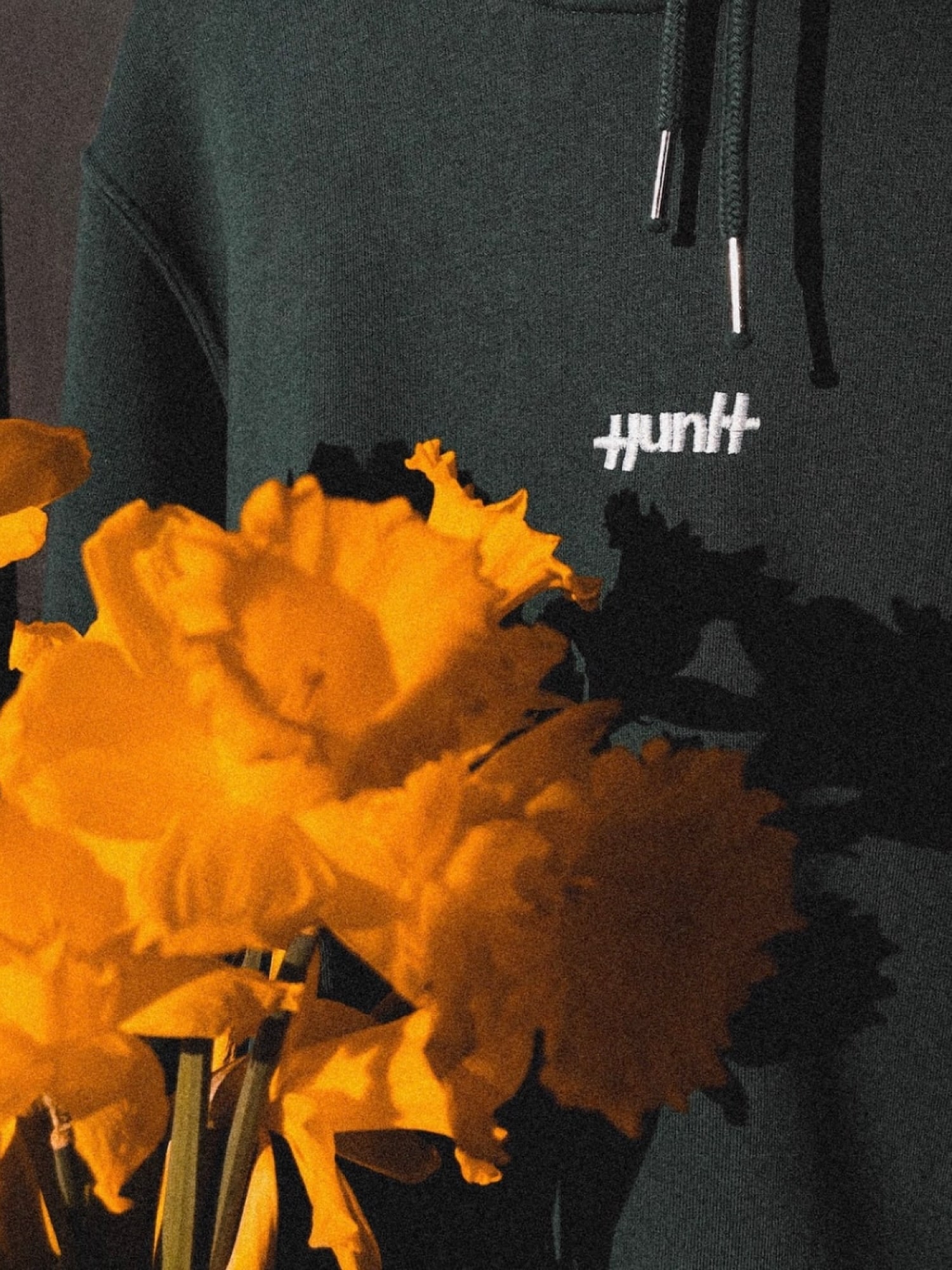 Yellow flowers in front of a green hoodie with an embroidered white Huntt logo