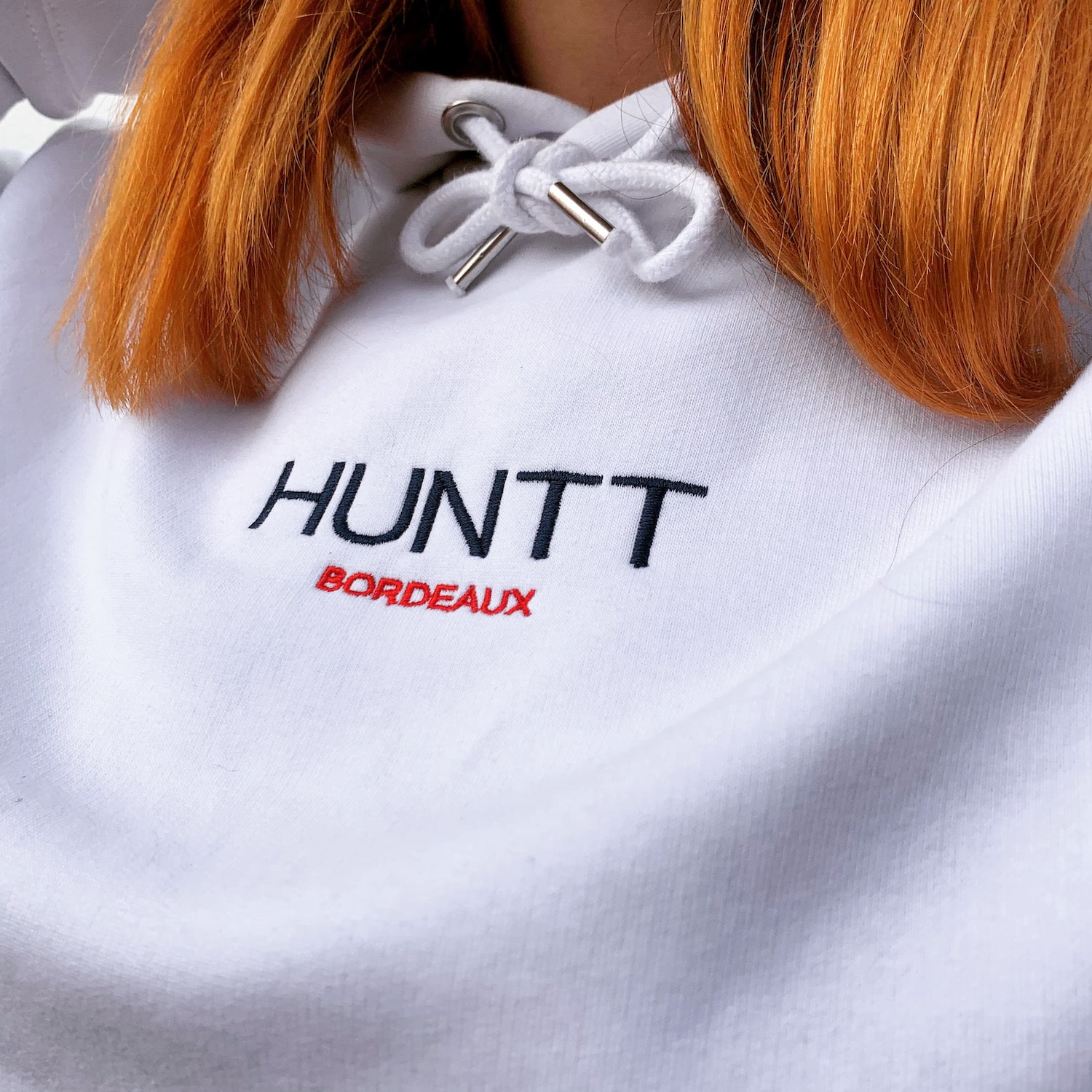 A woman wearing a white hoodie with Huntt Bordeaux embroidery